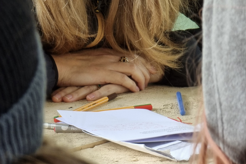 Person with arms folded in front of them, and before them there is a booklet with pencils and pens scattered around it on a table
